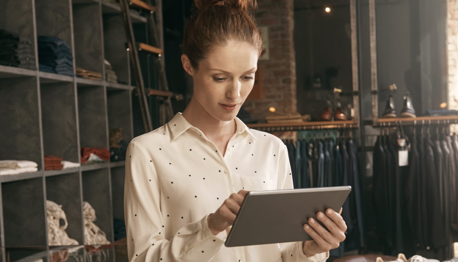 Osoba v obchodě s oblečením, která se dívá na tablet, pravděpodobně čte zpětnou vazbu od zákazníků